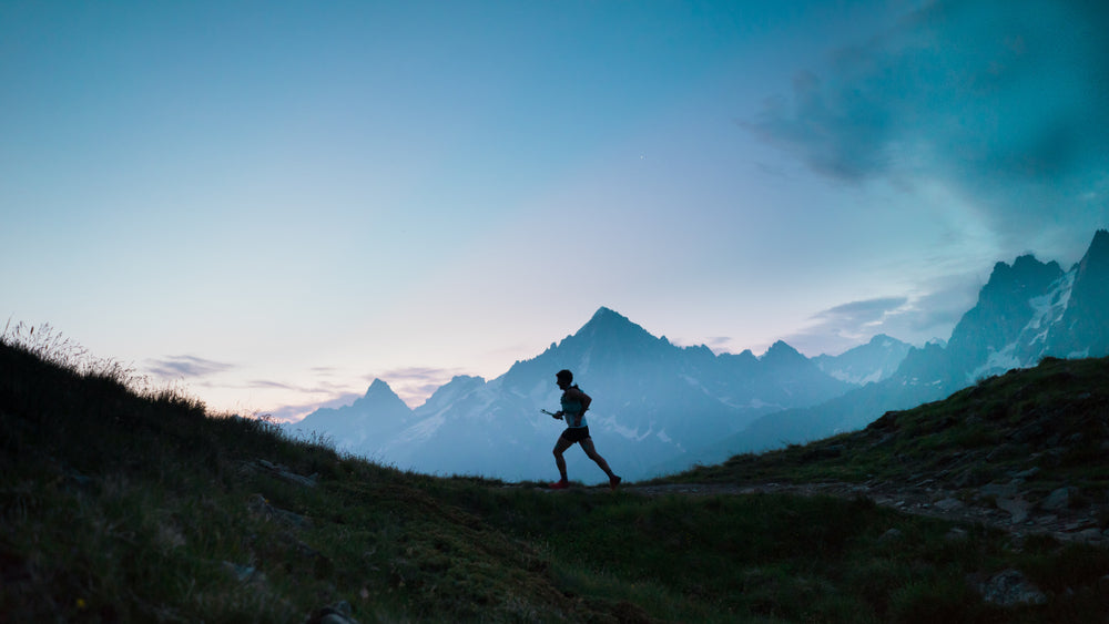 Silhouette of a person running on a mountain trail with a mountain range in the background